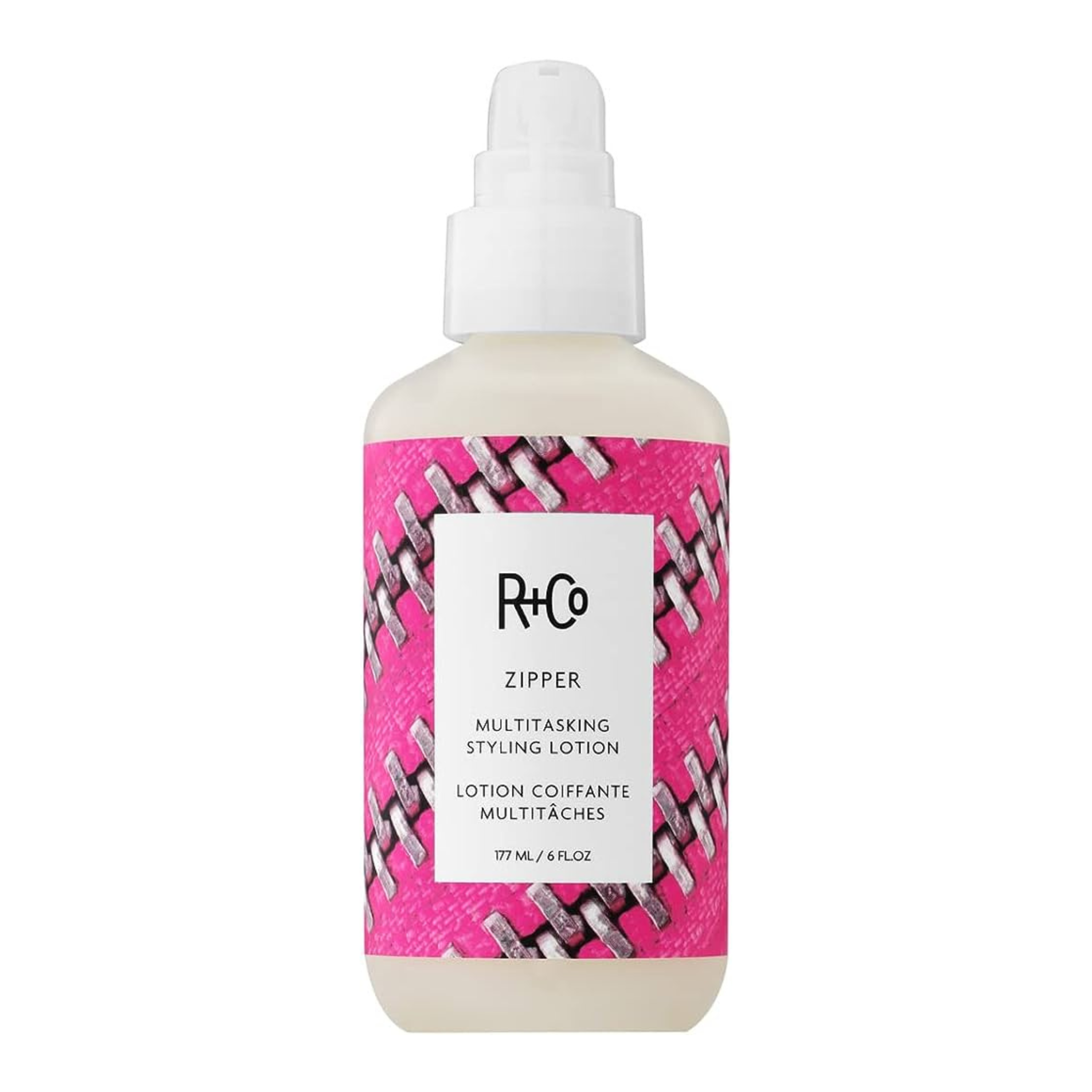 A bottle of R+Co Zipper Multitasking Styling Lotion with a pink and white design on the label.
