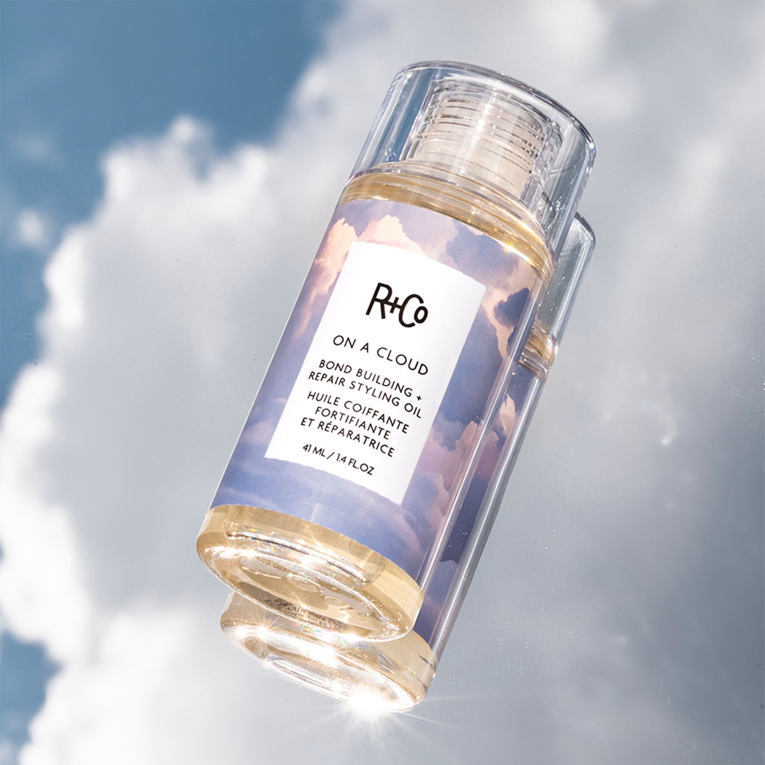 R+Co hair oil bottle with a cloud background