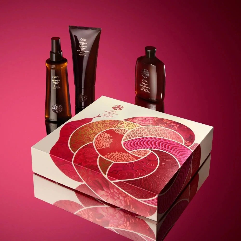 A set of Oribe magnifying hair care products including shampoo, conditioner, and maximista thickening spray, presented in a custom-crafted box with a decorative pattern.