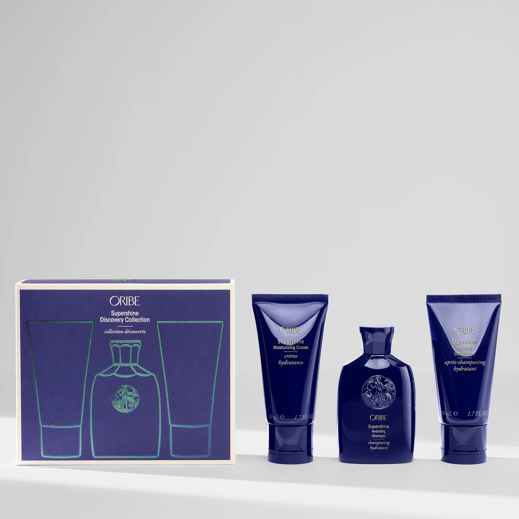 Oribe Supershine Discovery Collection set including a travel-sized Supershine Hydrating Shampoo bottle, a travel-sized Supershine Hydrating Conditioner bottle, and a travel-sized Supershine Moisturizing Cream tube, all in a matching blue packaging with gold accents.