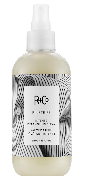 A bottle of R+Co Pinstripe Intense Detangling Spray with a black and white striped design on the label.