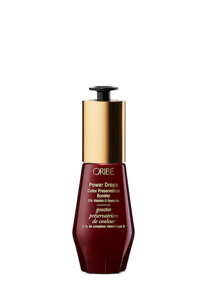 A bottle of Oribe Power Drops Color Preservation Booster, a hair care product with a red label and golden cap.