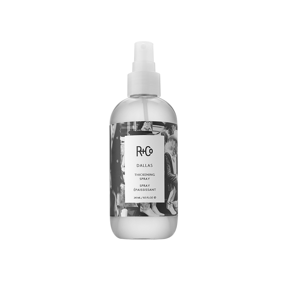 A white spray bottle labeled 'R+Co DALLAS Thickening Spray' with a transparent design showing the liquid inside.