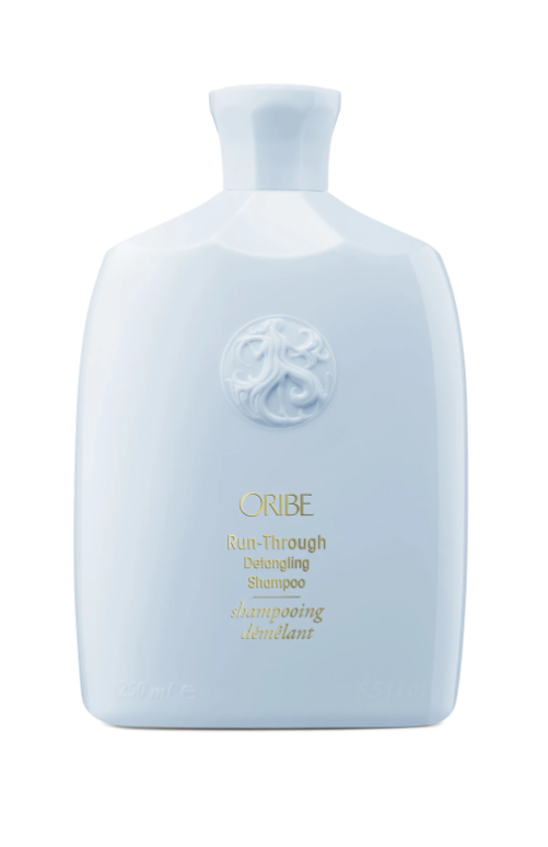 Bottle of Oribe Run-Through Detangling Shampoo with a white label and blue liquid.