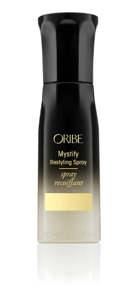 A black bottle of Oribe Mystify Restyling Spray with a white label and gold accents.