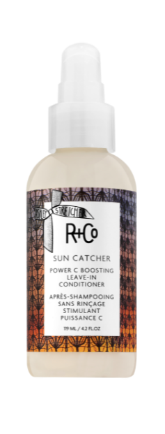 A bottle of R+Co Sun Catcher Power C Boosting Leave-In Conditioner with a dark background featuring a geometric pattern.
